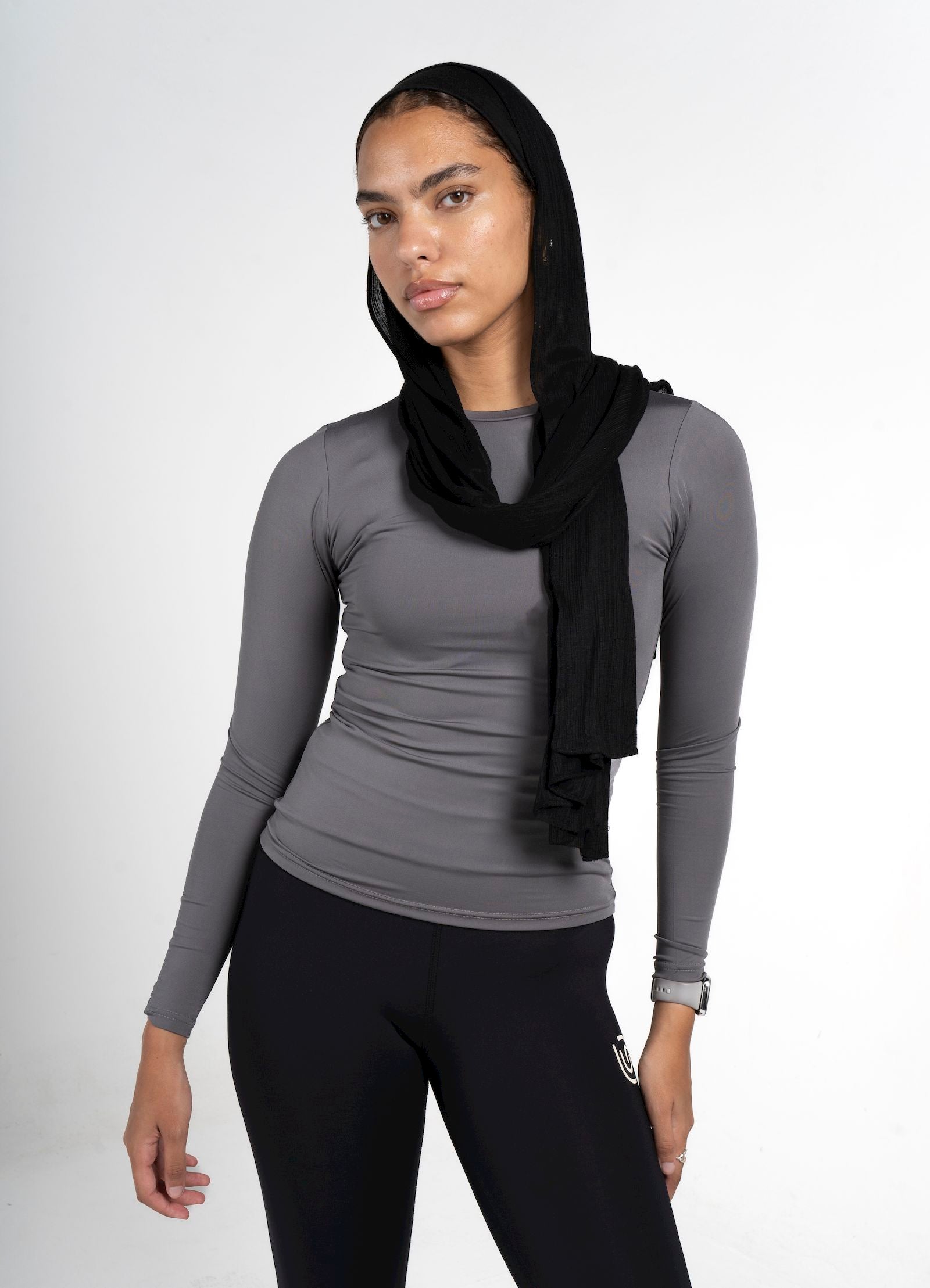 Person wearing a gray long-sleeve top and black leggings with a black hijab on a white background